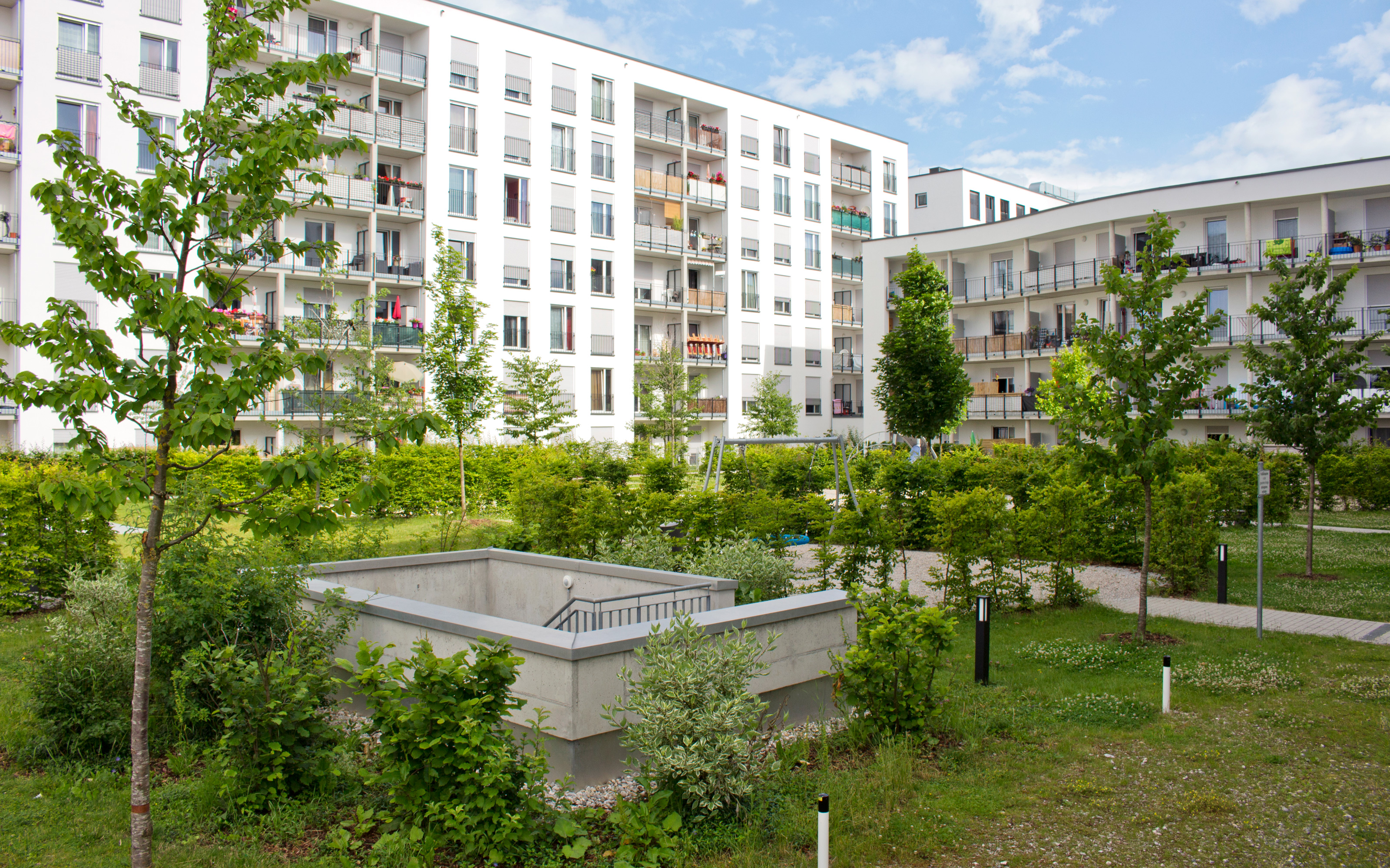 Park mit Rasen und kleinen Bäumen, umgeben von Mehrfamilienhäusern